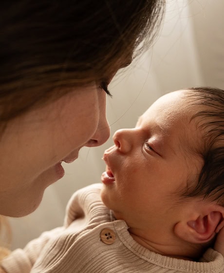 Un primer plano de una mujer sosteniendo a un bebé, ambos mirándose y pareciendo compartir un momento tierno.